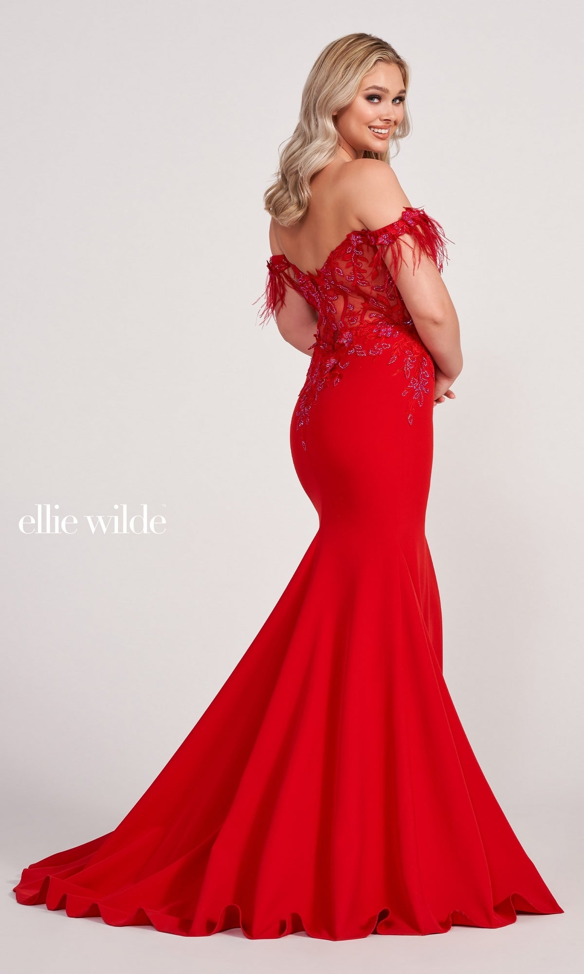A woman poses in the Ellie Wilde Feathered Off-Shoulder Long Prom Dress with embroidered details and a flared train, set against a plain background.